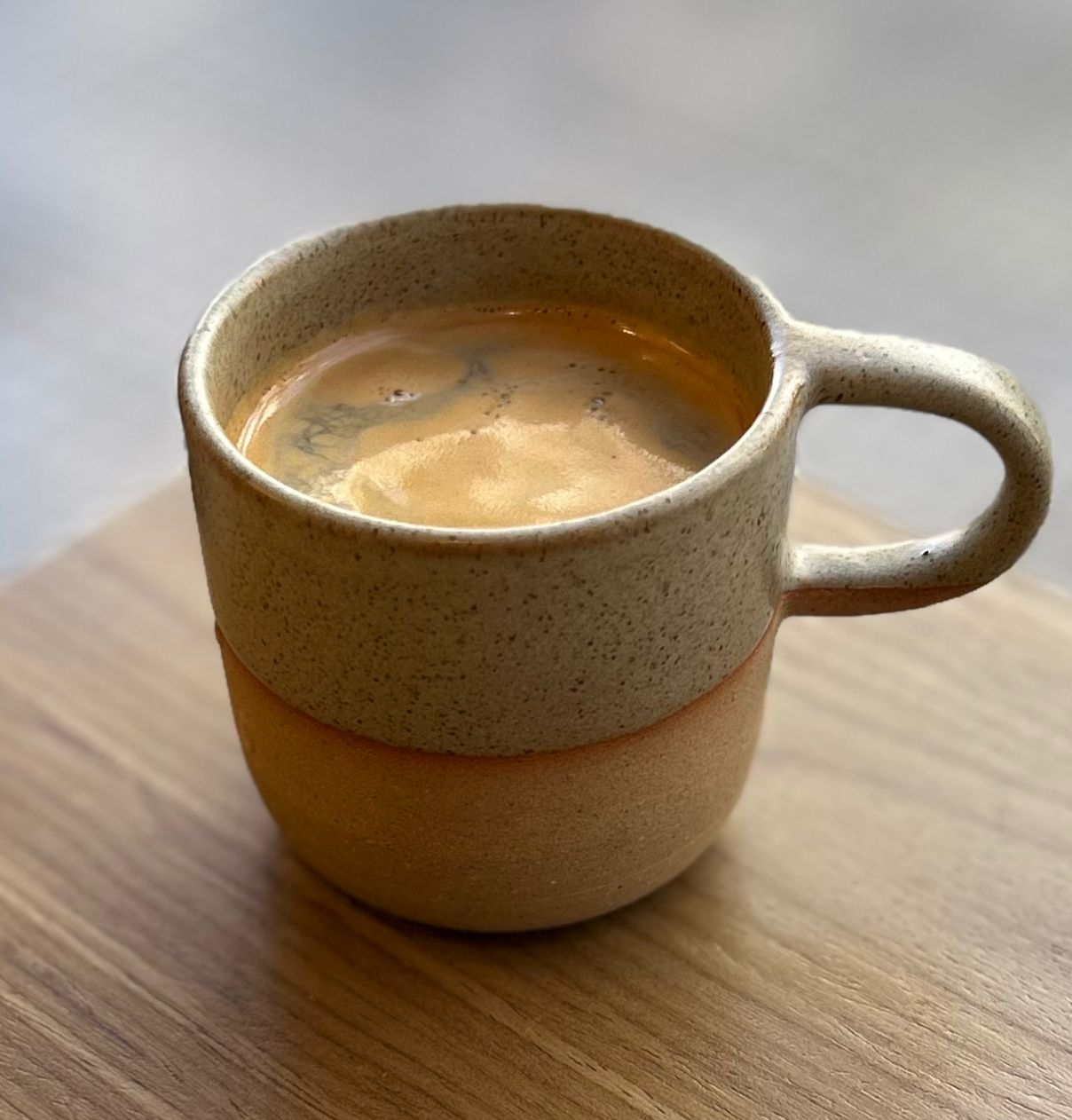 Americano en taza de cerámica moteada sobre mesa de madera