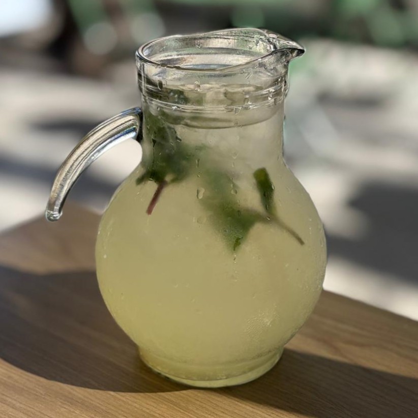 Jarra de vidrio con limonada y menta sobre mesa de madera